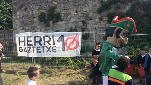 Varios-niños-y-un-cabezudo-de-la-comparsa-del-Casco-Viejo-conviven-con-un-cartel-del-movimiento-okupa-durante-las-fiestas-de-San-Fermín-de-Aldapa.