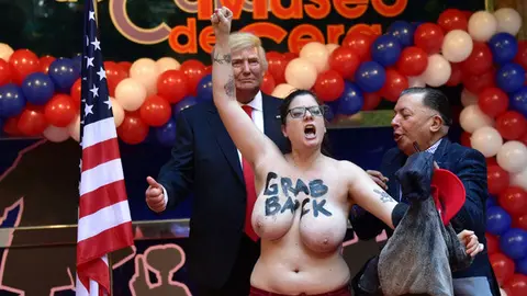 Madrid's Wax Museum director Gonzalo Presa (R) tries to protect the wax statue of US President-elect Donald Trump from a topless Femen activist protesting in Madrid on January 17, 2017. / AFP PHOTO / GERARD JULIEN