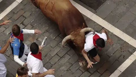 GRA020. PAMPLONA, 13/07/2017.- Un toro de la ganadería gaditada de Núñez del Cuvillo arrolla a un mozo en el tramo inicial de la calle Estafeta, durante el séptimo encierro de los San Fermines 2017, en el que las reses han protagonizado una rápida carrera de dos minutos y diez segundos hasta la arena de la plaza, y en la que, hasta el momento, se han contabilizado dos heridos por asta y un contusionado. EFE/Juan Pedro Urdíroz