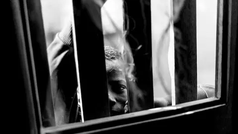 Un niño talibé observa a través de una ventana con rejas. La educación de los talibés está basada en amenazas, violencia y castigos. Los niños sufren desde golpes y latigazos hasta la privación de libertad por varios días o semenas y en ocasiones atados con cuerdas y grilletes. IÑIGO ALZUGARAY