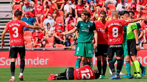 Los jugadores del RCD Mallorca hablan con el árbitro mientras su compañero Iddrisu Baba (c) se encuentra tendido en el suelo ante el futbolista del Osasuna Brasanac (c, arriba), durante su partido de LaLiga disputado este domingo en Palma de Mallorca. EFE/Cati Cladera