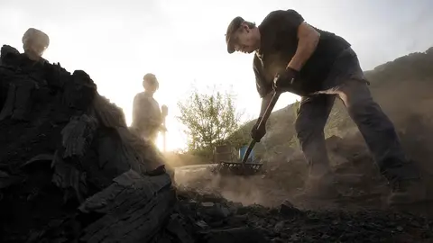 En las faldas de la abrupta y vertiginosa sierra de Lokiz, todavía huele a carbón. Ese olor a leña cocida, que inundó el pueblo y todo el valle de Lana hasta mediados del siglo XX, ahora solo proviene de las carboneras de Miguel que ayudado por su mujer Mertxe y su hijo Arkaitz son los últimos carboneros que realizan tan ancestral oficio. Aprovechan el verano para cocer madera de encina como se hacía antaño, orgullo identitario del valle. El carbón que se produce de la madera de los encinares comunales de la zona será combustible en los mejores asadores de todo el país. Una carbonera de estas dimensiones tarda en cocerse unos 15 días durante los que hay que vigilarla continuamente e ir añadiéndole  “betagarri“ (madera para que no se produzcan vacíos). EFE/ Jesús Diges