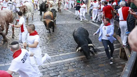 Un mozo cae sobre un toro en el segundo encierro de San Fermín 2024 con toros de Cebada Gago en la curva de Mercaderes. MIGUEL FERNÁNDEZ / KUKUXUMUSU
