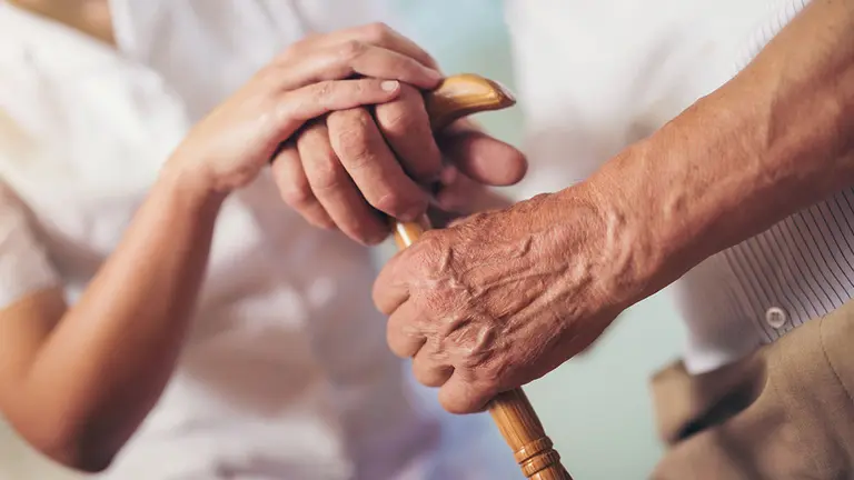 Una cuidadora ayuda a caminar a una persona mayor con un bast&oacute;n. ARCHIVO