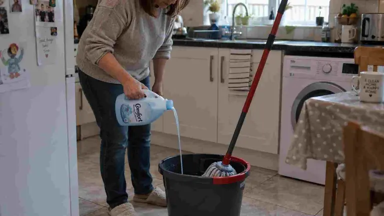 Una mujer echando suavizante en el cubo de fregar en la cocina de su casa.