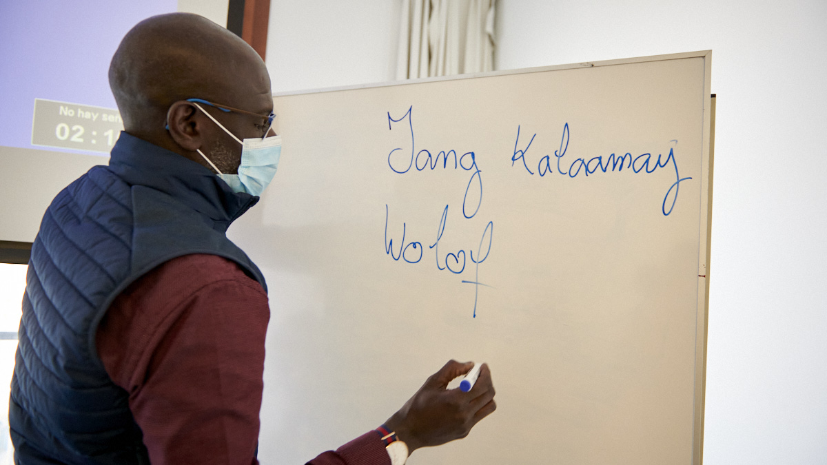Abou Diouf escribe la frase "Yo estuido wolof" en la pizarra. IRANZU LARRASOAÑA