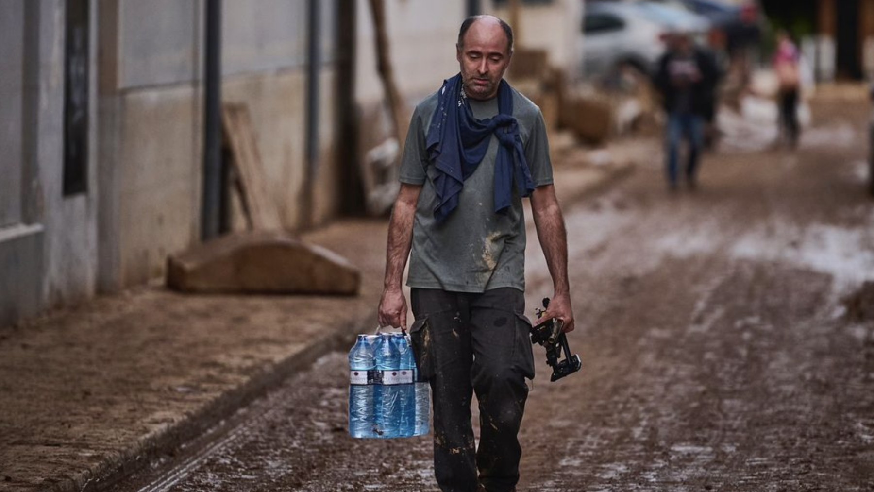 Un hombre camina por una calle, arrasada por la Dana en Valencia, con unas botellas de agua y un gesto de agotamiento y tristeza. PABLO LASAOSA