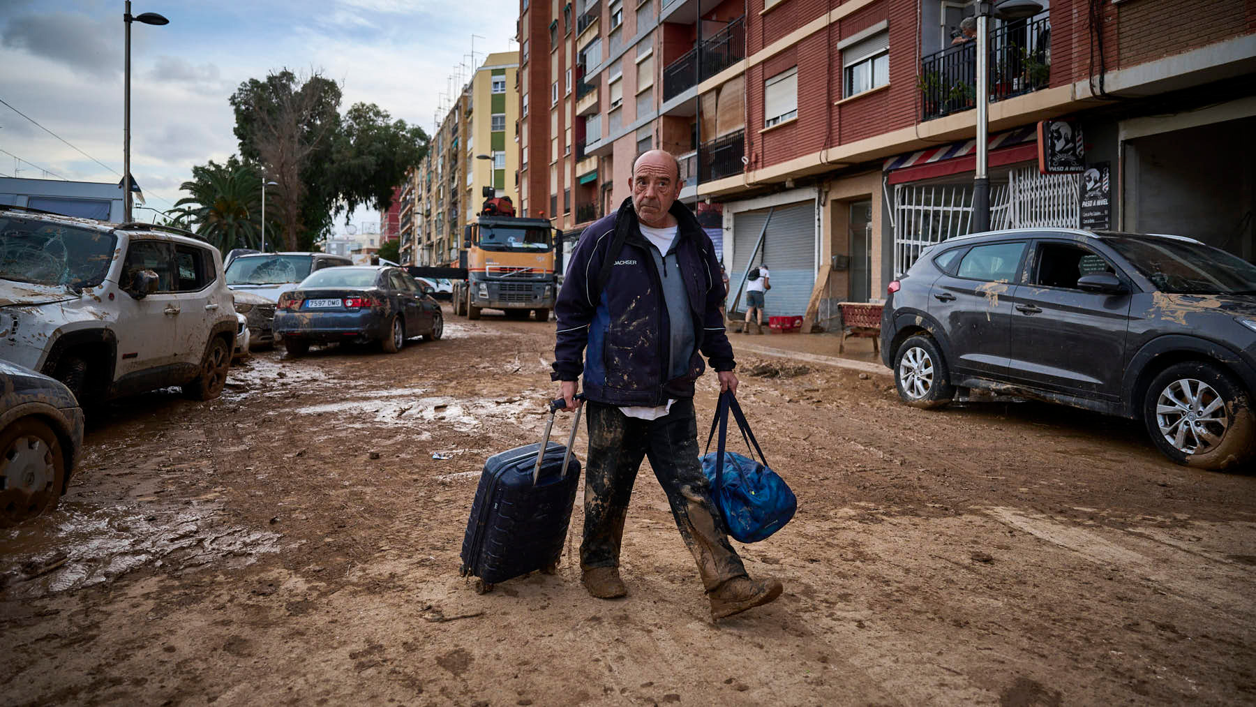 Un hombre camina con una maleta y una bolsa por las calles de Benetúser. PABLO LASAOSA