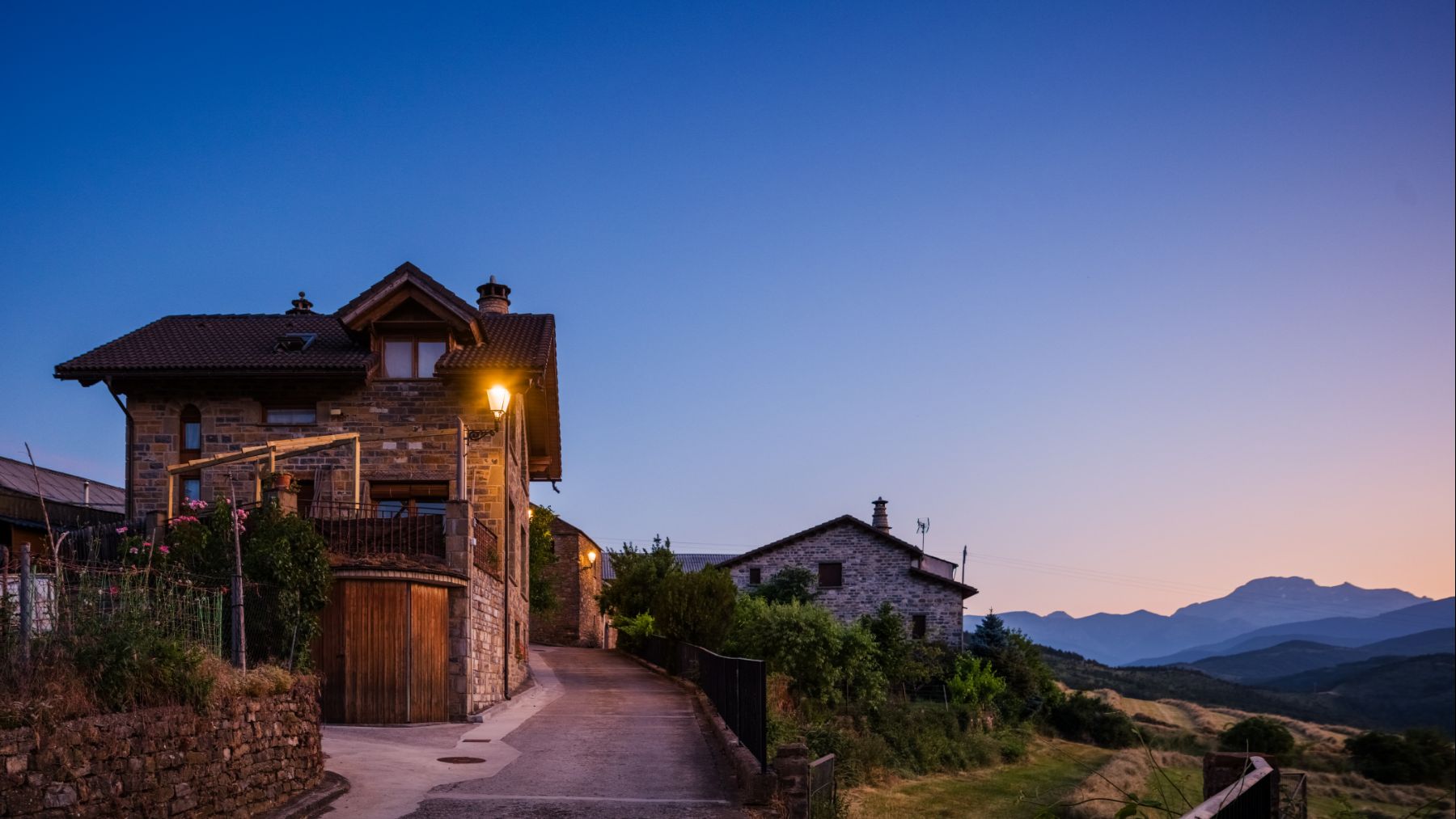 Transición del día a la noche en Sinués, con luminarias clásicas Villa XLA integradas en la arquitectura del valle de Aísa. ATP ILUMINACIÓN