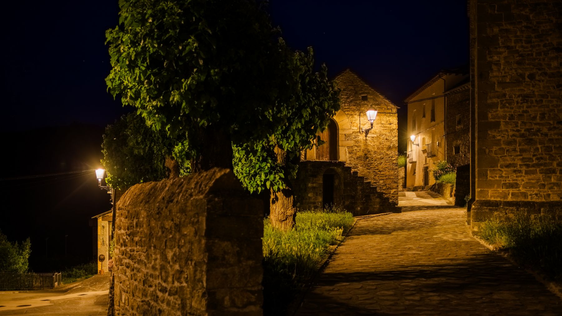 Iluminación uniforme y cálida que realza las fachadas de piedra y refuerza la identidad rural del entorno.. ATP ILUMINACIÓN